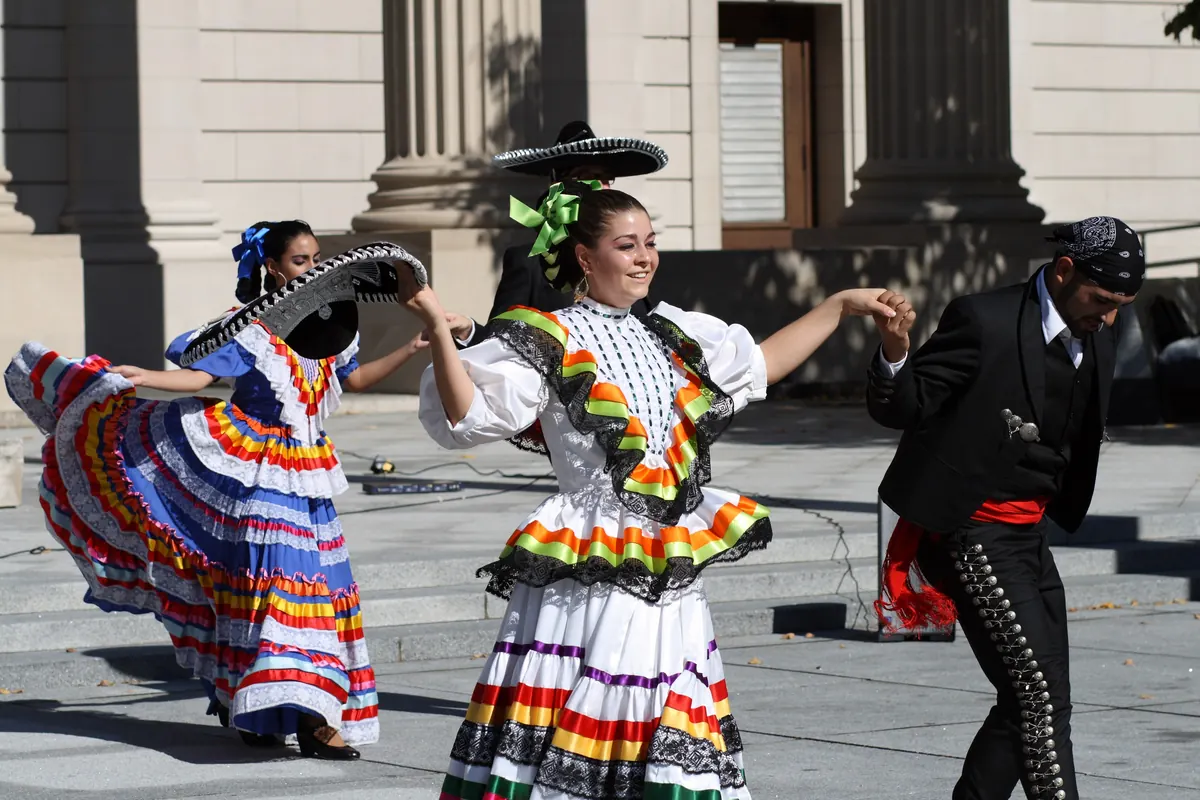 Folklórico dancers spinning wide striped skirts beside a dancer in a charro suit