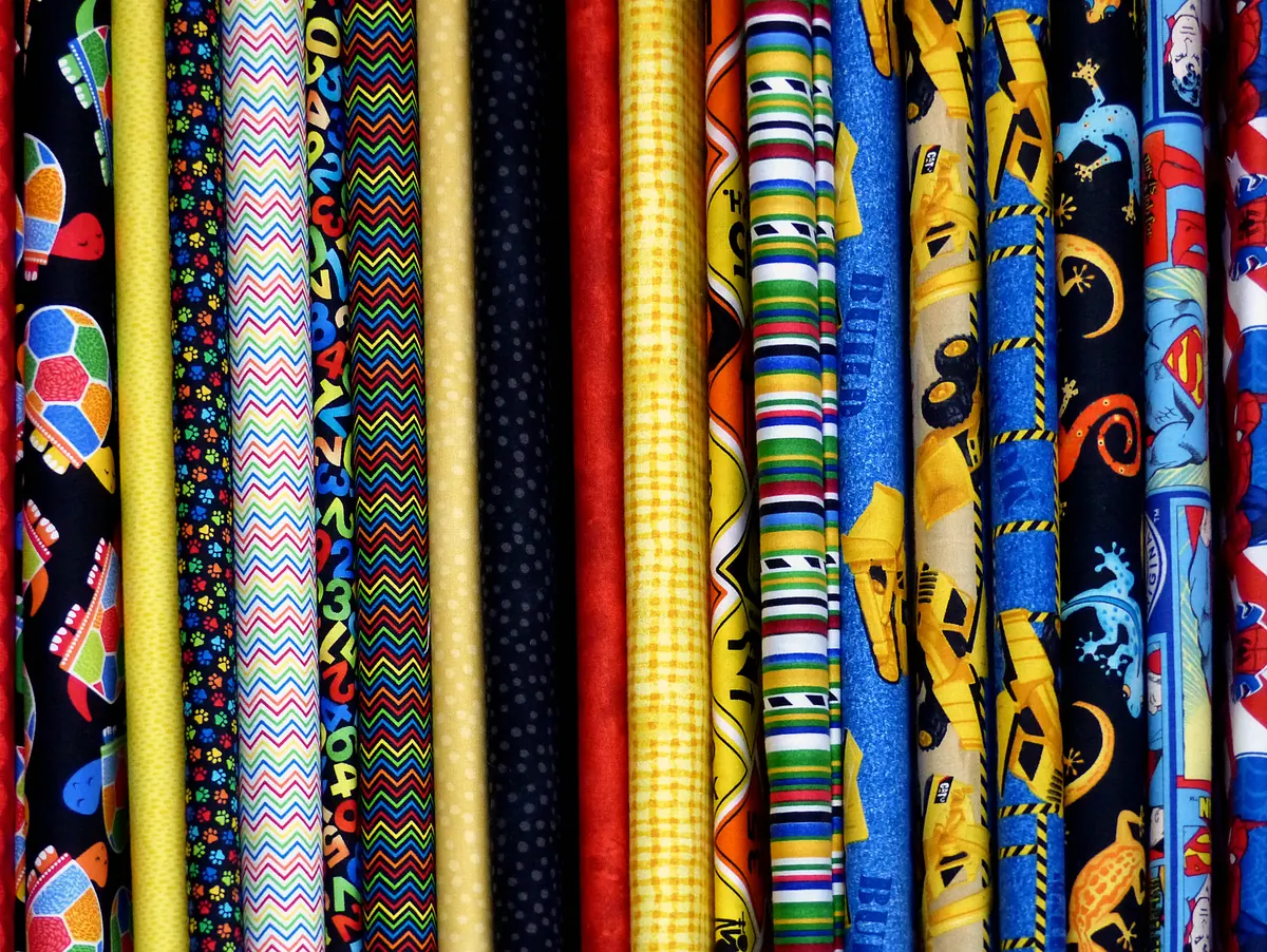 Rolls of bright printed fabric standing side by side on a shop shelf