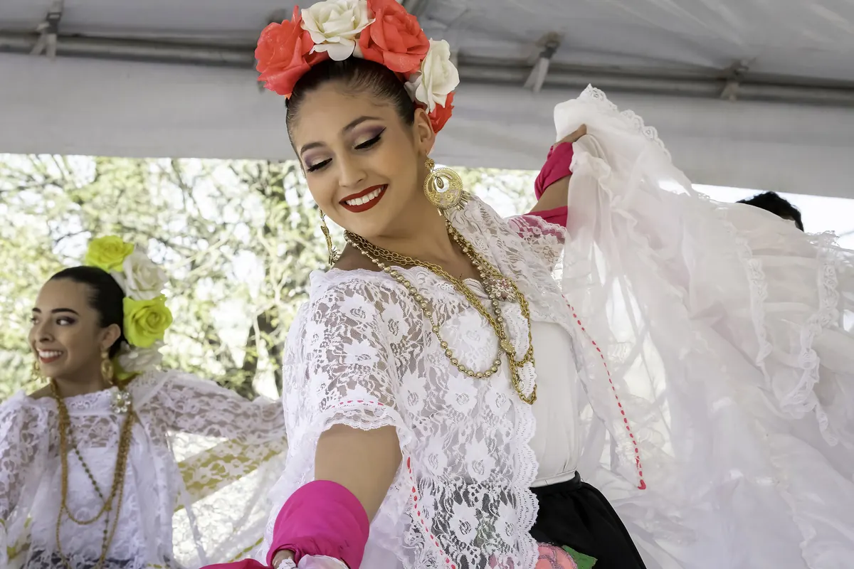 A folklórico dancer in a white lace Veracruz dress and red flowers in her hair
